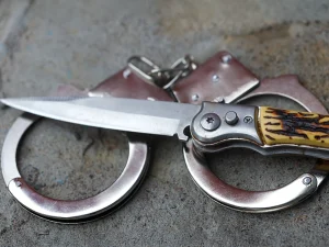 Close-up of a folding knife lying on metal handcuffs, symbolizing violent crime charges and stand your ground legal issues in a Tampa murder trial.