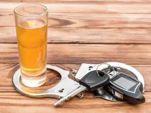 Shot glass in handcuffs beside car keys, symbolizing criminal history mistakes in state drunk driving punishment