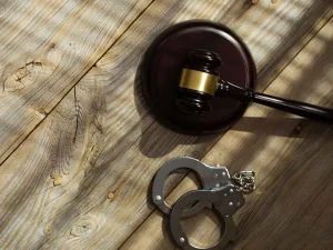 Judge gavel beside metal handcuffs on rustic table symbolizing punishment after offense labeled serious crime