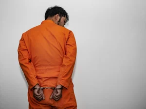 Handcuffed man in an orange prison uniform standing against a wall, representing evidence sufficient to prove a probation violation in Florida