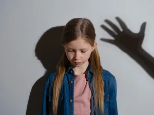Sad young girl standing against wall with a threatening hand shadow, symbolizing child abuse allegations and lesser included sex crime charges in Florida