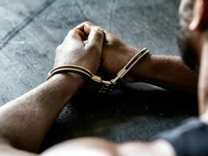 Person’s hands in handcuffs resting on a dark table