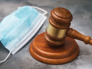 Wooden judge gavel beside medical face mask symbolizing prison term modification requests during coronavirus surge