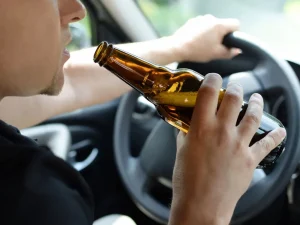Man drinks beer while driving car, representing legal debates about roadside stops and rights of DUI defendants