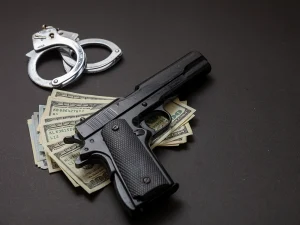 Handcuffs and a handgun resting on U.S. dollar bills against a dark background, symbolizing criminal court proceedings and jury-related legal issues