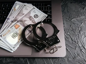 handcuffs and cash on a laptop keyboard representing restitution in florida theft and fraud cases