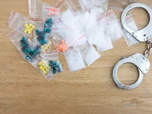 Plastic baggies of illegal drugs next to handcuffs on wooden table