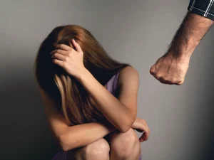 Terrified young woman cowering on the floor as a fist is raised, symbolizing abuse and child hearsay evidence in Florida sex crime cases